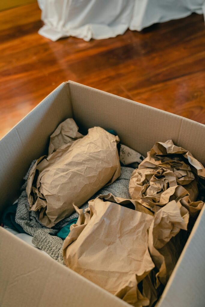 From above of open cardboard box on wooden floor full of things wrapped in packaging paper prepared for moving in new apartment