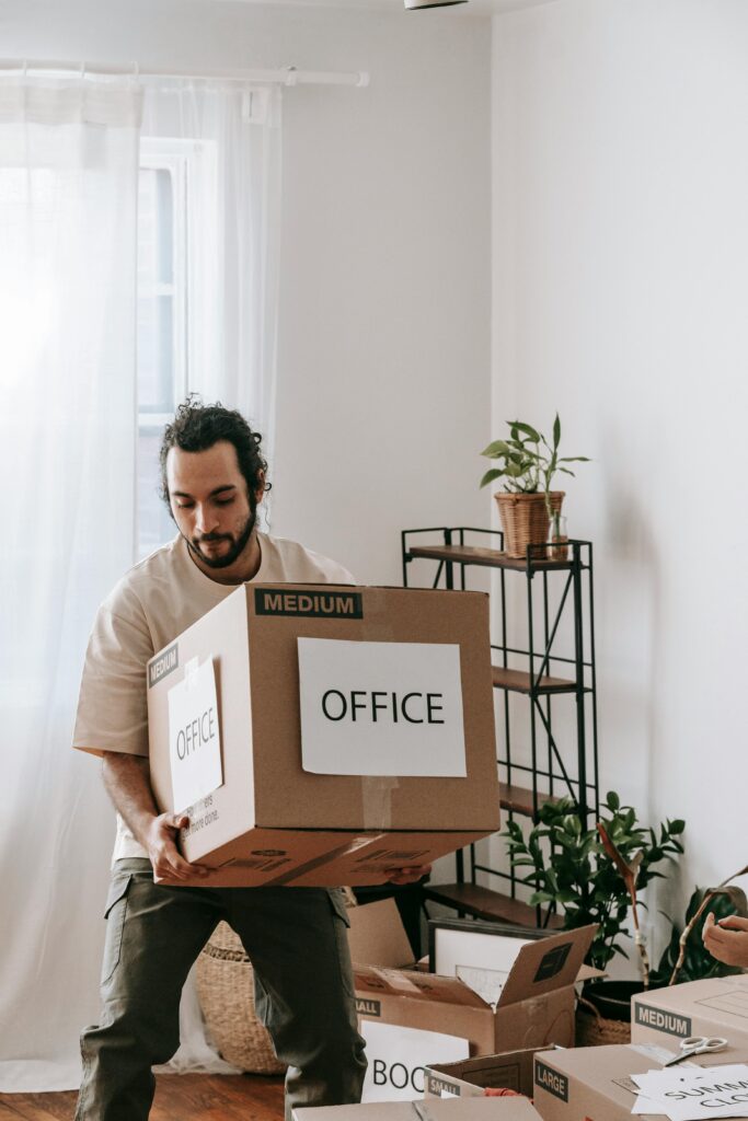 Young man carrying boxes while moving office in a modern apartment setting.